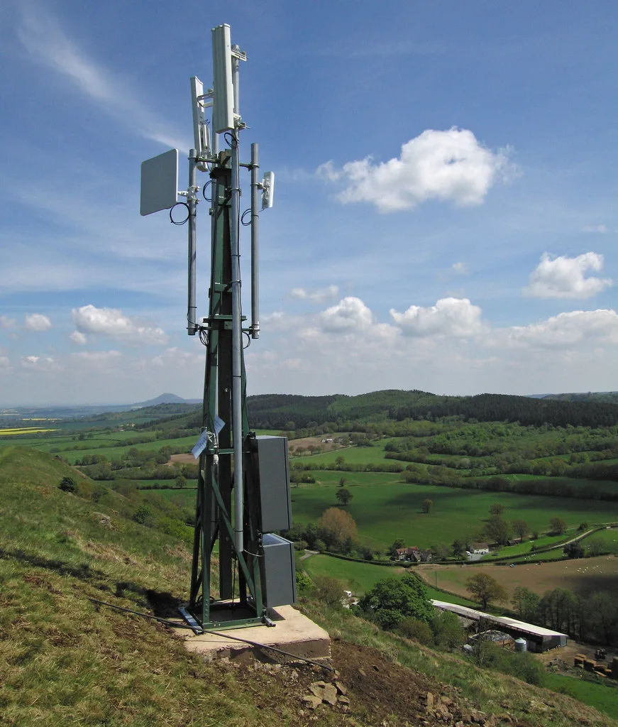 A slim radio mast with panel antennas on a hillside above green Shropshire farmland
