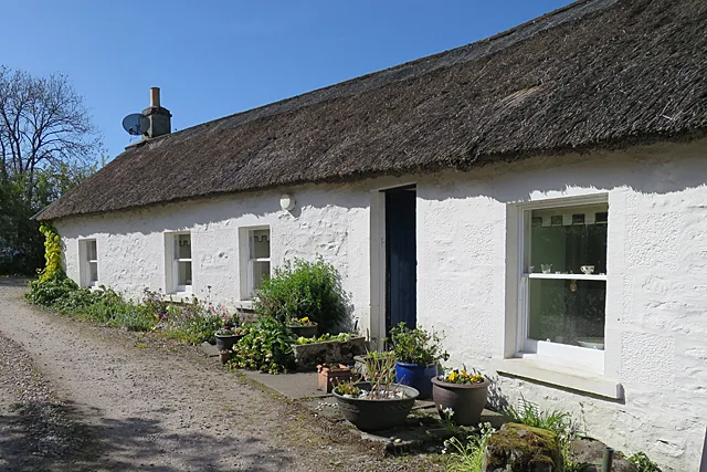 A white-painted thatched cottage with a satellite dish on its chimney