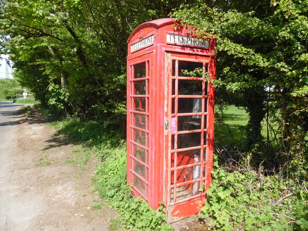 A red K6 telephone box beside a country lane, half hidden by hedges