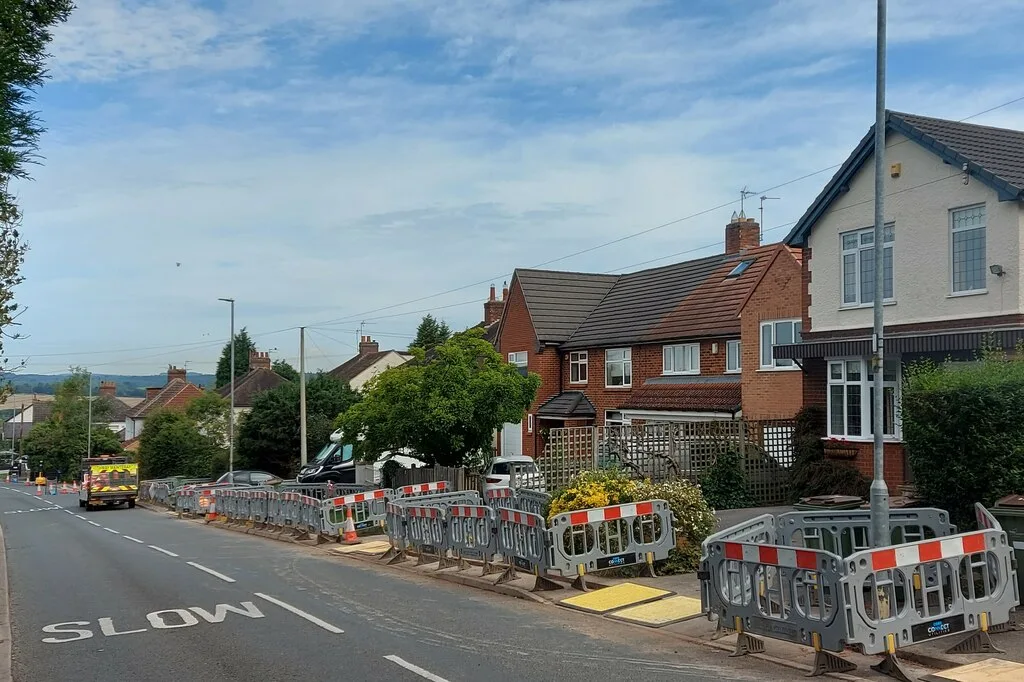 Barriers along the pavement of a suburban street of brick houses while fibre-optic cable is laid